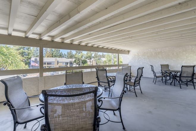 An outdoor covered patio with multiple tables and chairs arranged for seating.