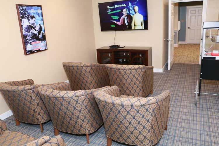 A cozy seating area with patterned chairs facing a television on the wall.