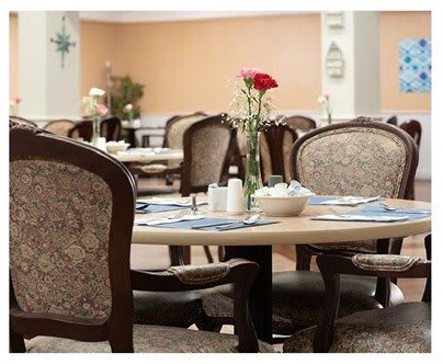 An elegant dining room with tables set and a rose centerpiece.