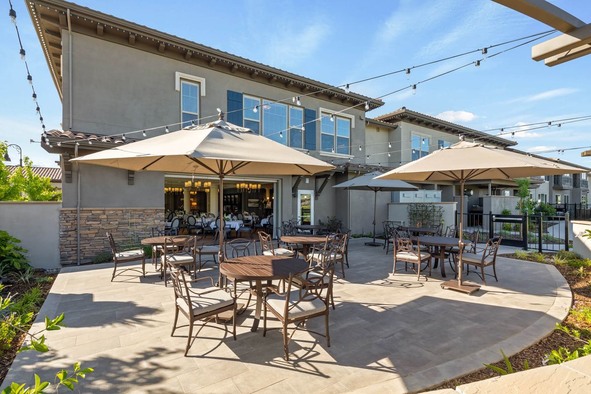 An outdoor patio with tables, chairs, and umbrellas at a cafe or restaurant on a sunny day.