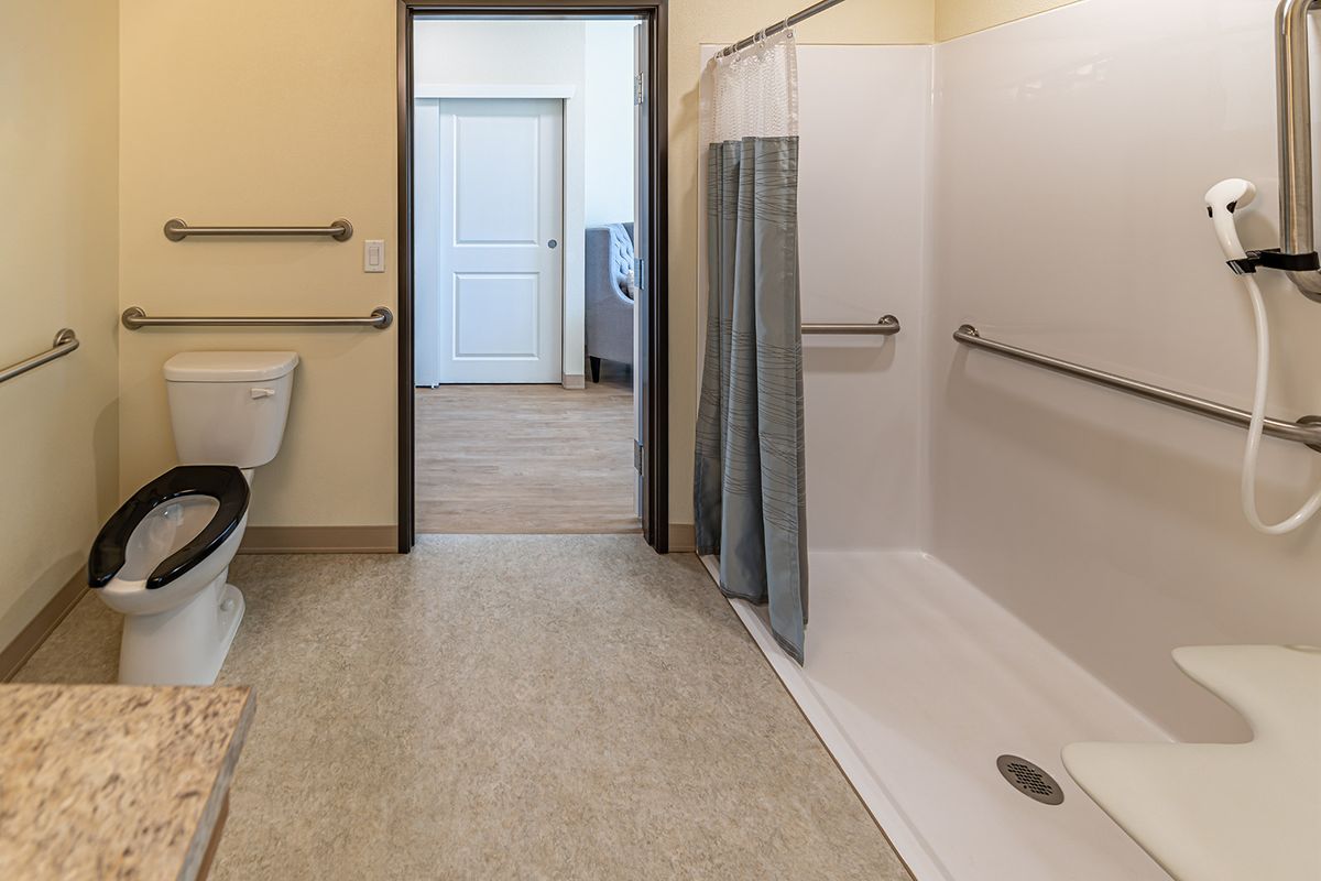 An accessible bathroom featuring a walk-in shower with grab bars and a curtain, alongside a sink with an open design.