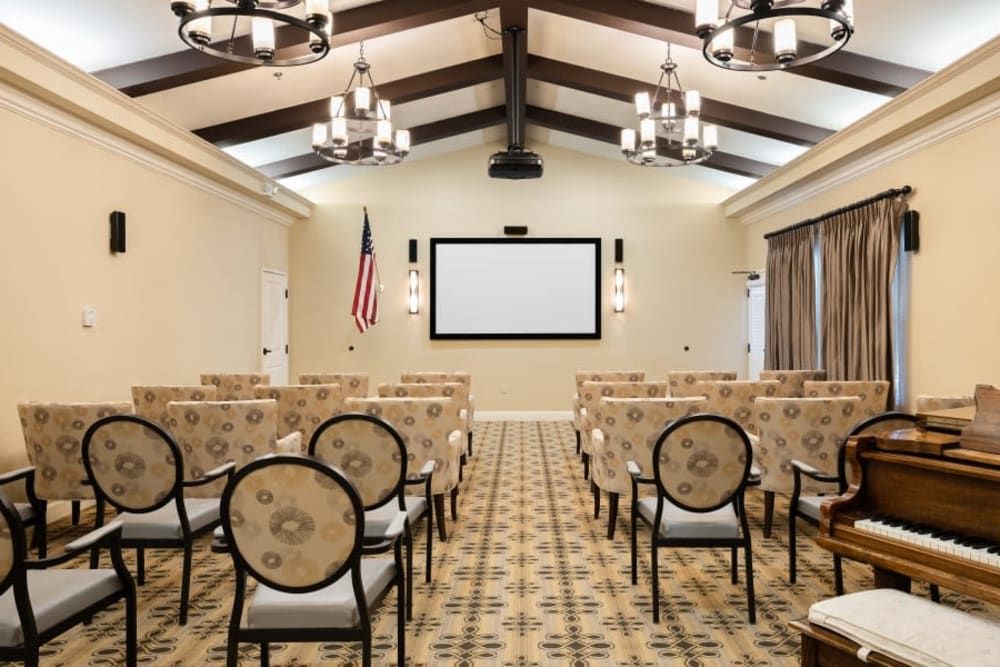 A conference room with rows of chairs facing a large screen, adorned with chandeliers and an American flag.