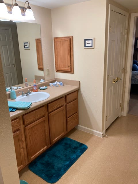 A bathroom with a sink, mirror, and wooden cabinets, featuring teal towels and a bath mat.