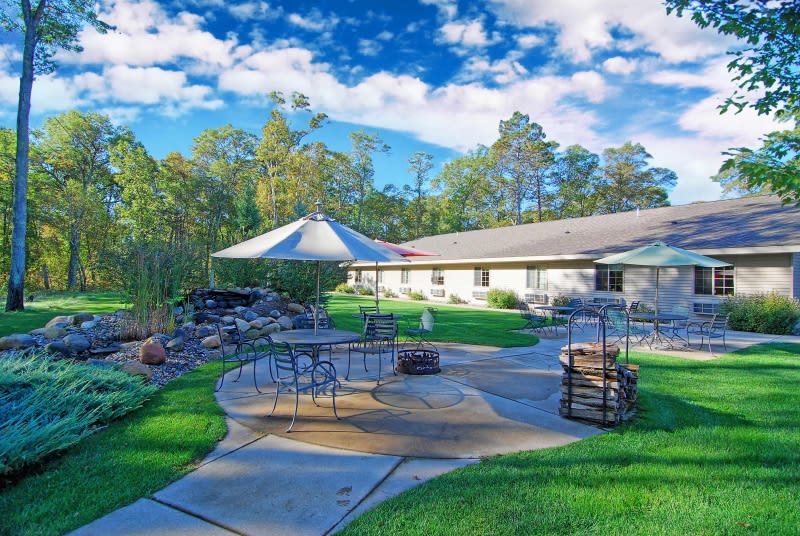 A beautiful backyard patio with outdoor seating and a large umbrella, surrounded by lush greenery.