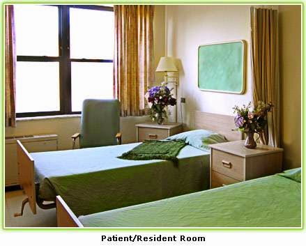A serene patient/resident room featuring two beds, green bedding, and a touch of floral decor.