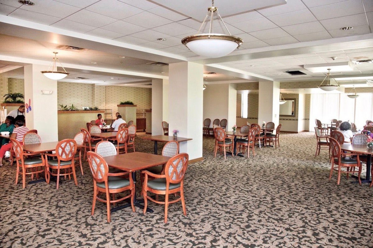 A spacious dining area with multiple tables and chairs, featuring patterned carpet and overhead lighting.