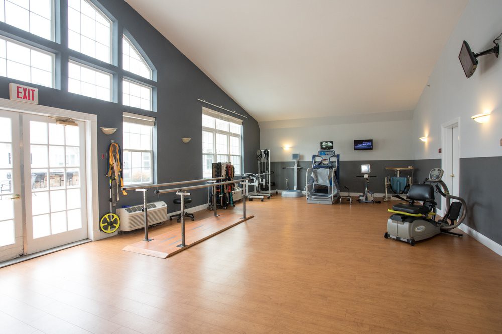 A well-lit rehabilitation therapy room with exercise equipment and large windows.