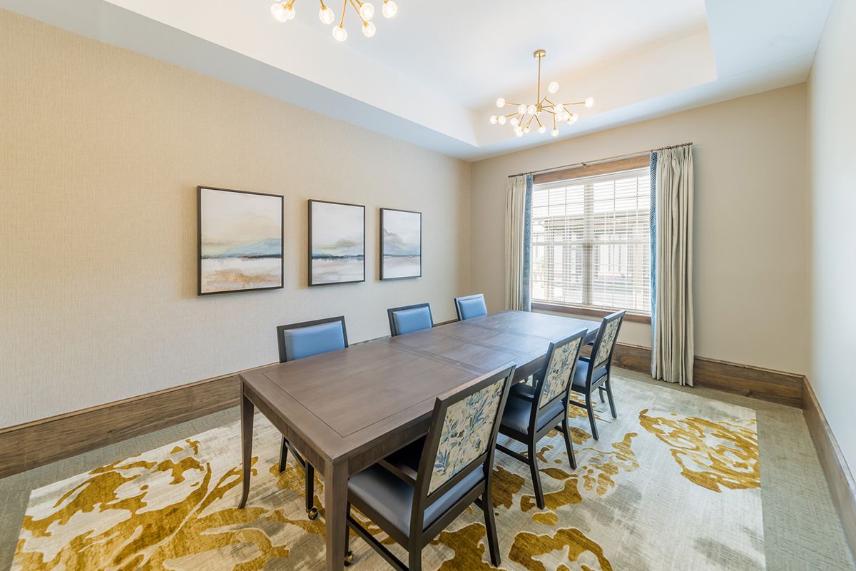 A spacious dining room featuring a large table with chairs, framed artwork on the wall, and natural light streaming through a window.