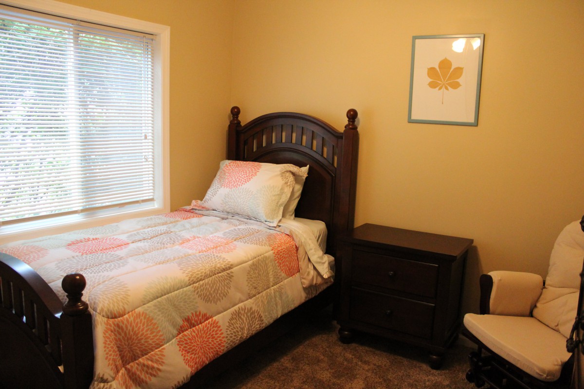 A cozy bedroom featuring a single bed with a patterned comforter, a nightstand, and wall art.