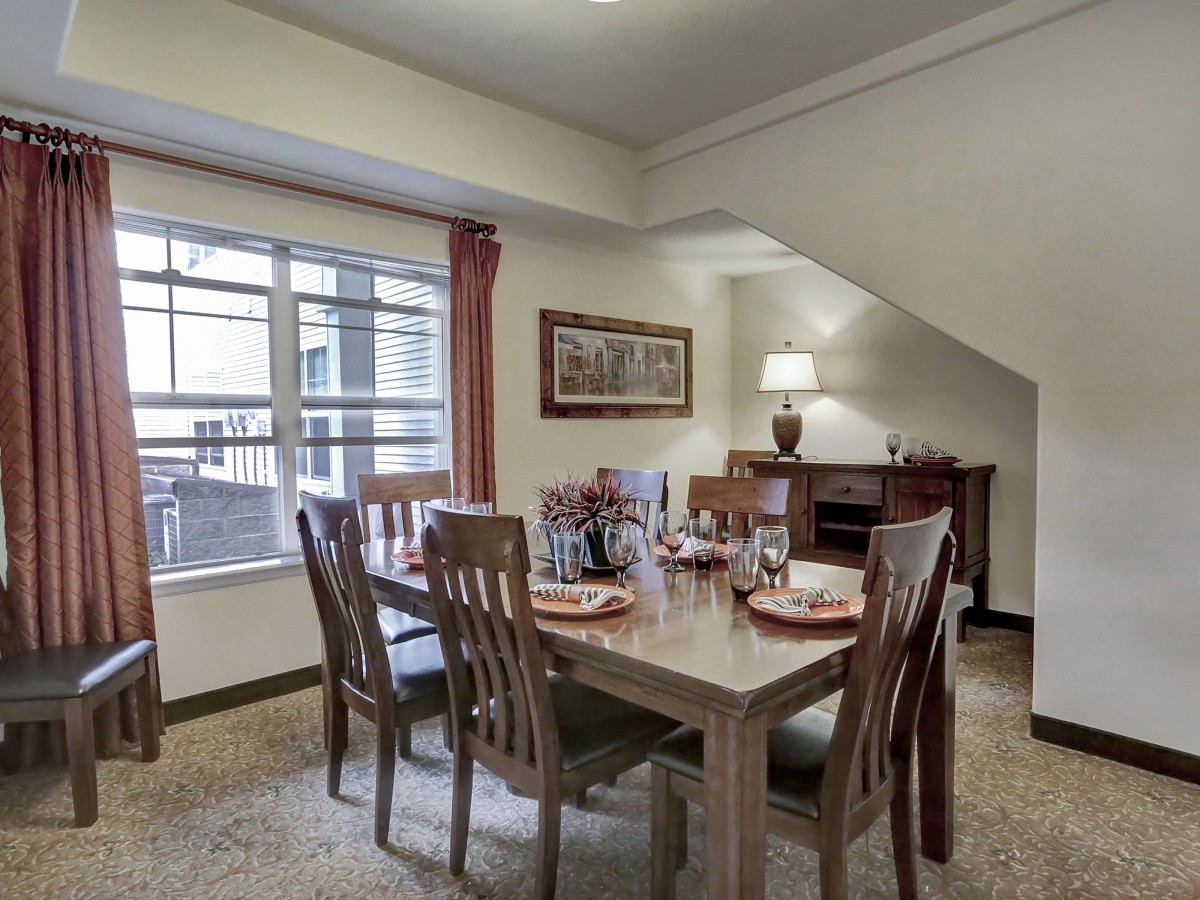 A cozy dining room with a wooden table set for a meal, illuminated by natural light from the window.
