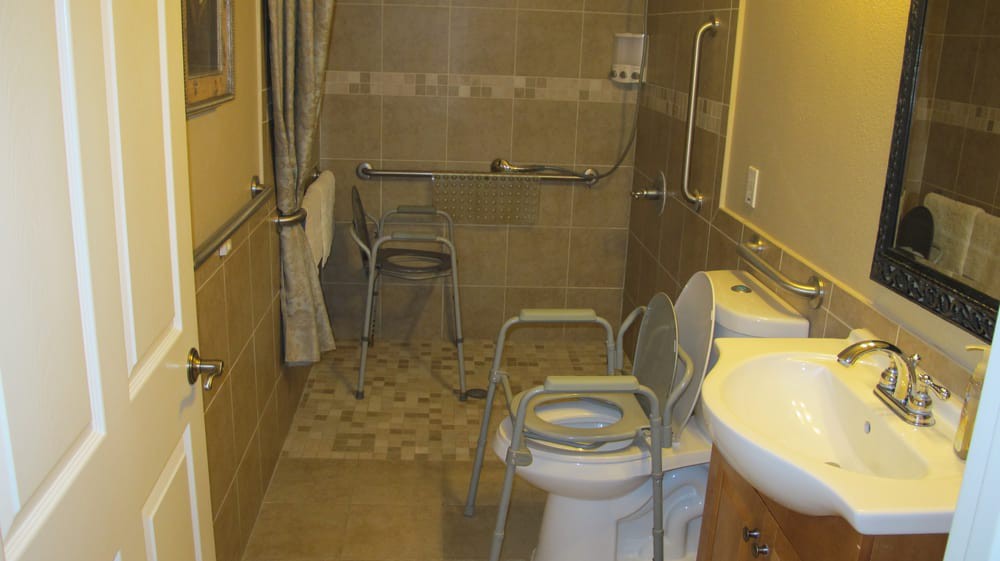An accessible bathroom equipped with grab bars, a commode chair, and a shower area.