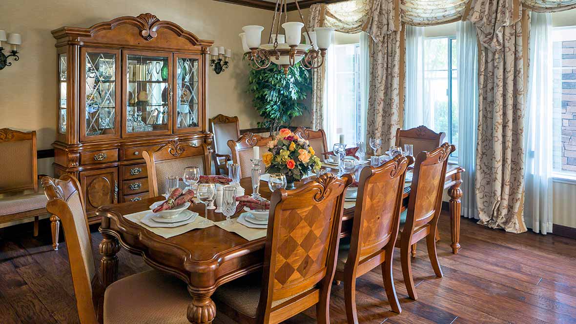A beautifully set dining table with elegant wooden chairs, a chandelier overhead, and decorative curtains enhancing the ambiance.