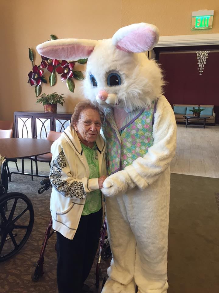 An elderly woman hugs a person in an Easter Bunny costume indoors.