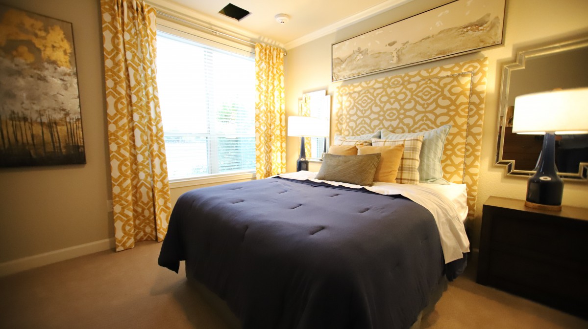 A well-decorated bedroom featuring a large bed with pillows and a dark comforter, surrounded by patterned curtains and soft lighting.