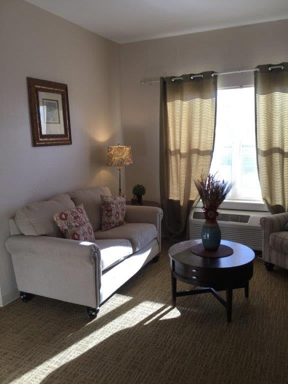 A cozy living room with a sofa and armchair arranged around a coffee table, illuminated by a standing lamp near the window.