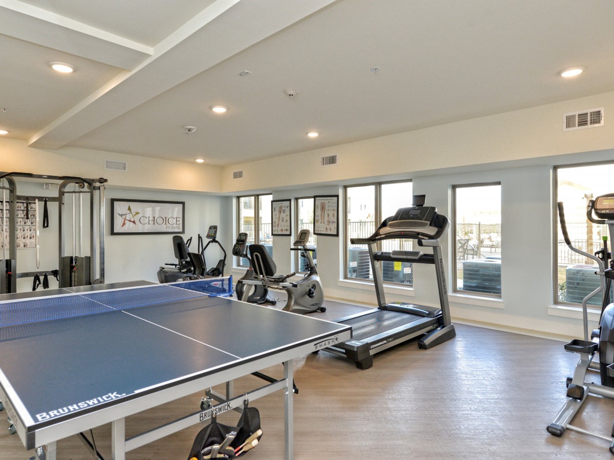 A well-equipped gym featuring treadmills, ellipticals, stationary bikes, and a ping pong table.