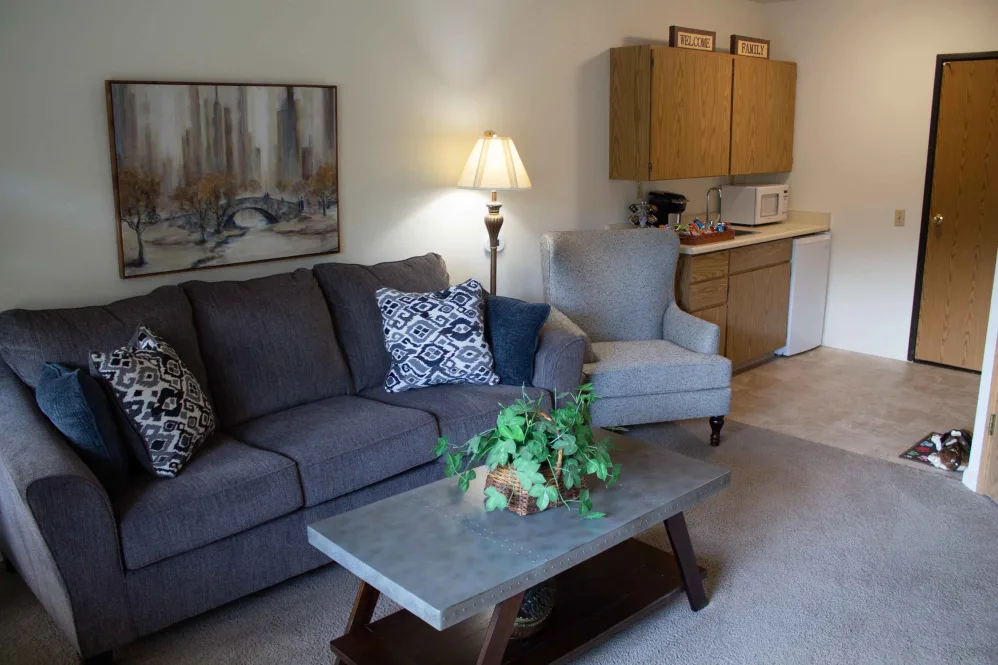 A cozy living room with a sofa, armchair, and coffee table, adjacent to a compact kitchen area.