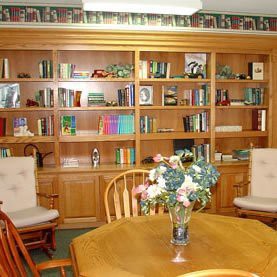 A cozy library room featuring a wooden bookshelf filled with books and a table with flowers.