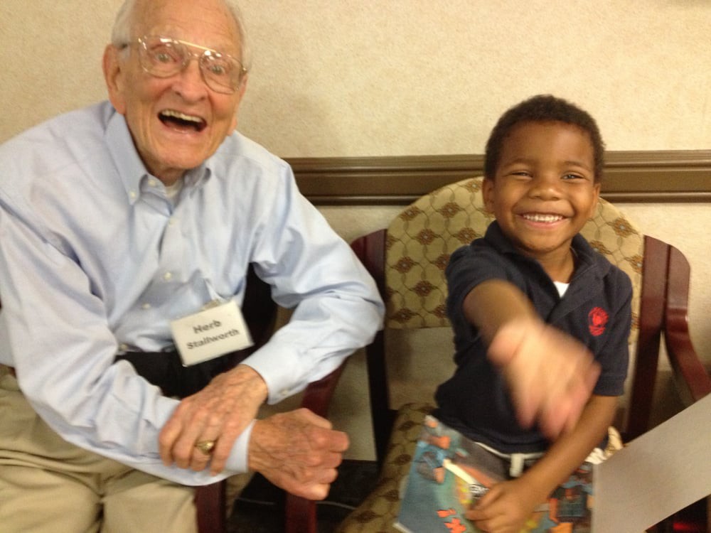 An elderly man and a young boy are sitting and sharing a joyful moment, both smiling broadly.