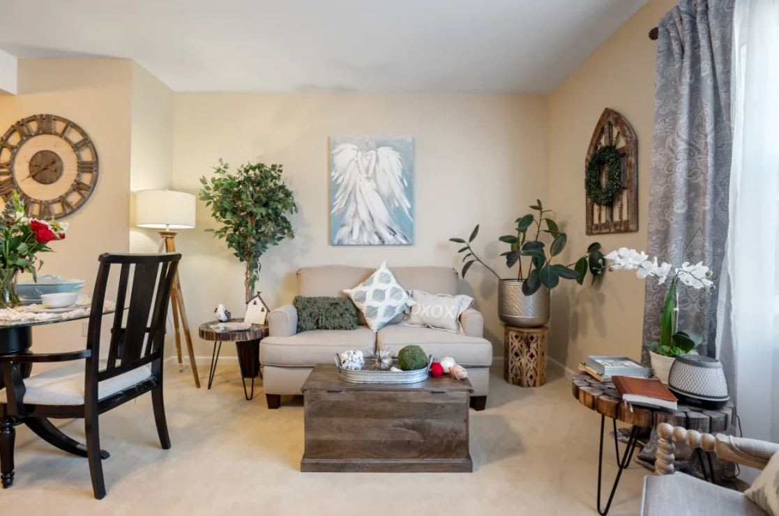 A cozy living room with a neutral sofa, decorative pillows, and indoor plants, featuring a coffee table and wall art.