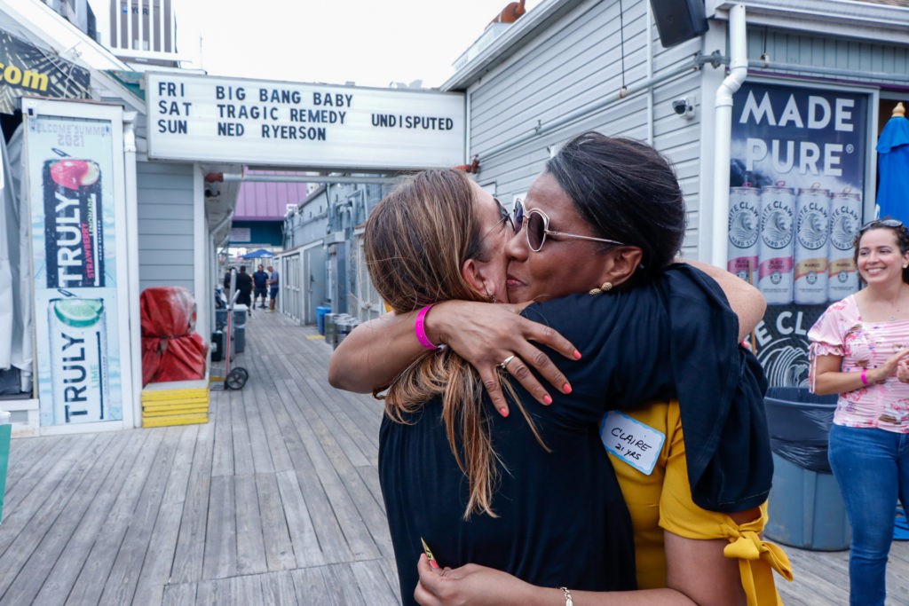 Two people embrace in a warm hug outside a building with a marquee sign.