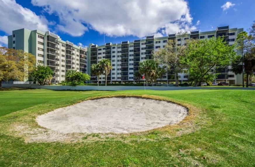 A view of an apartment building overlooking a golf course with a sand trap in the foreground.