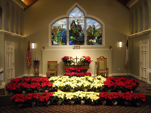 A beautifully decorated church altar adorned with red and white poinsettias, featuring a stunning stained glass window in the background.
