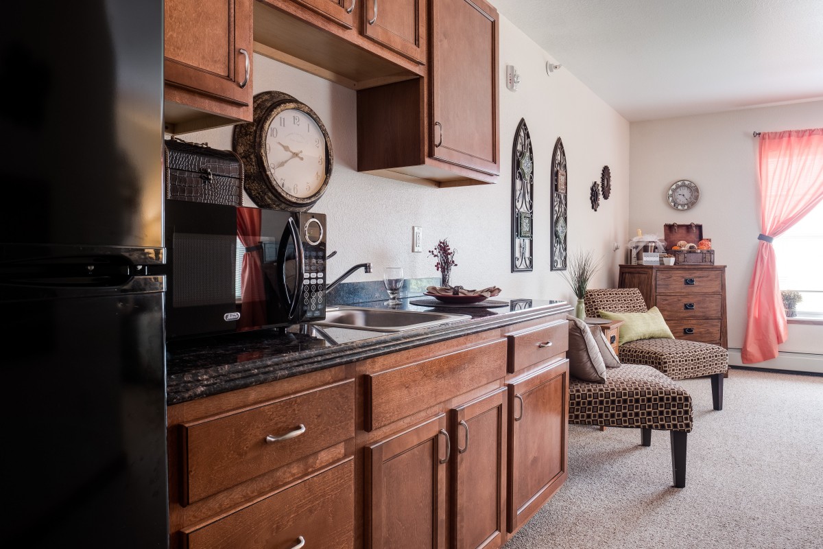 A cozy kitchen area with wooden cabinets and a coffee maker, blending into a living space.