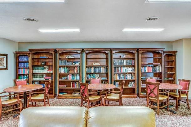 A cozy library reading area with wooden bookshelves, tables, and chairs.