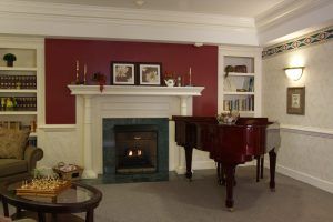 A cozy living room featuring a red accent wall, a white mantelpiece with a fireplace, and a glossy grand piano.