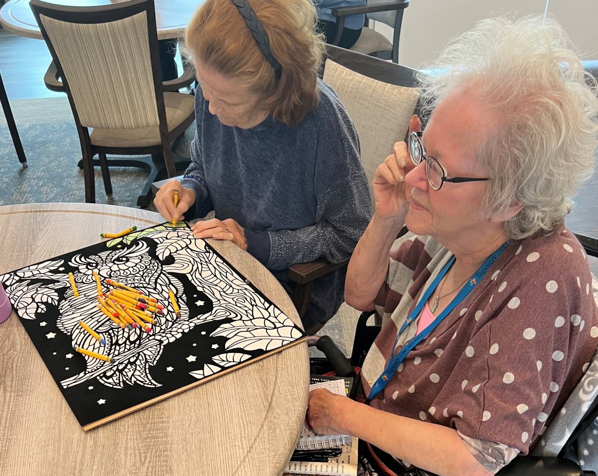 Two seniors engaged in a coloring activity at a table.