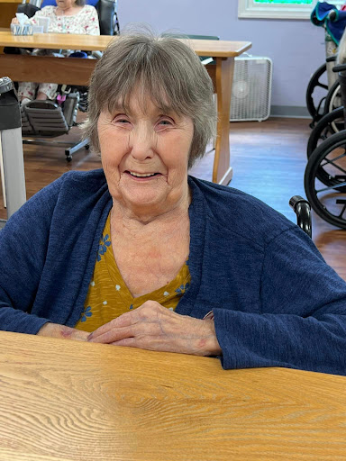 A joyful elderly woman sitting at a table in a care facility.