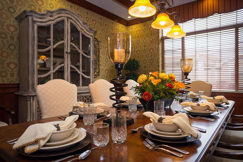 An elegantly set dining table with candles and floral centerpiece, surrounded by plush chairs and warm lighting.