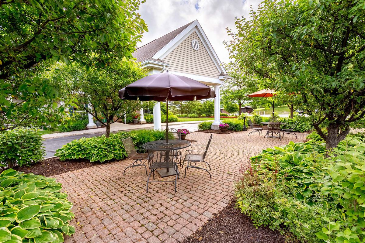 A peaceful garden patio with tables and umbrellas surrounded by lush greenery.