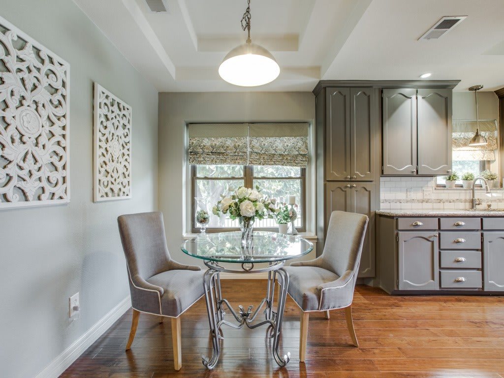 A modern dining area with a glass table and elegant chairs, featuring sleek cabinetry and a hardwood floor.