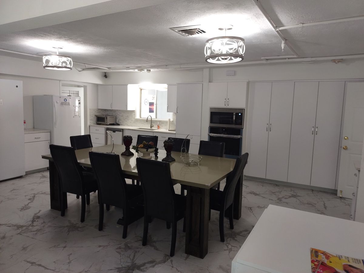 A modern dining area with a large table, multiple chairs, and a view of the kitchen.