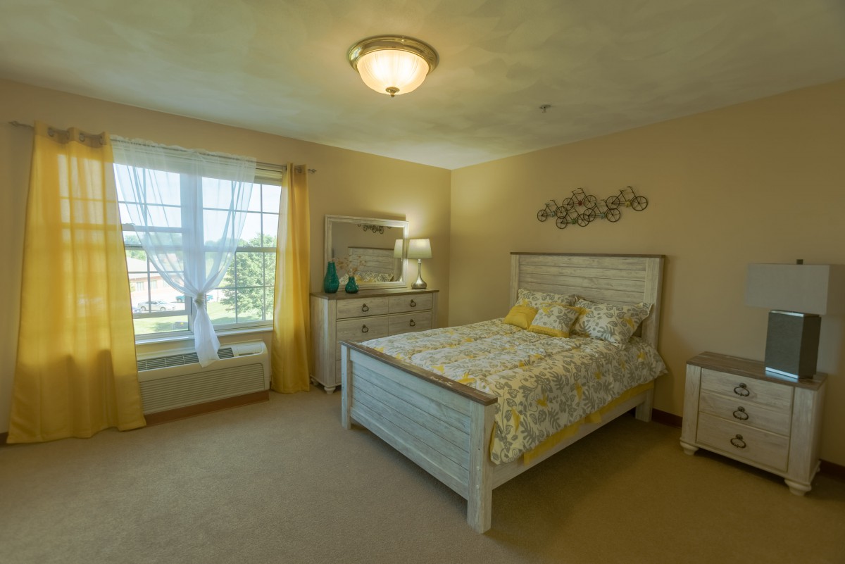 A cozy bedroom with a wooden bed, dresser, and bright yellow accents.