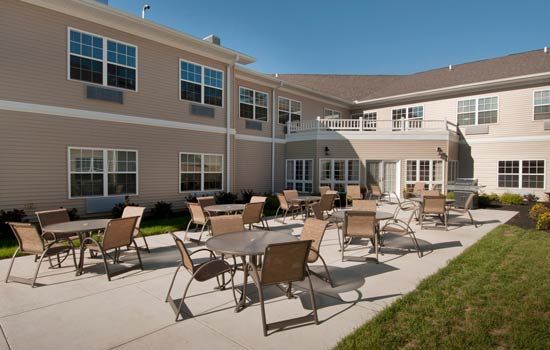 A sunny outdoor patio area with tables and chairs in front of a residential building.