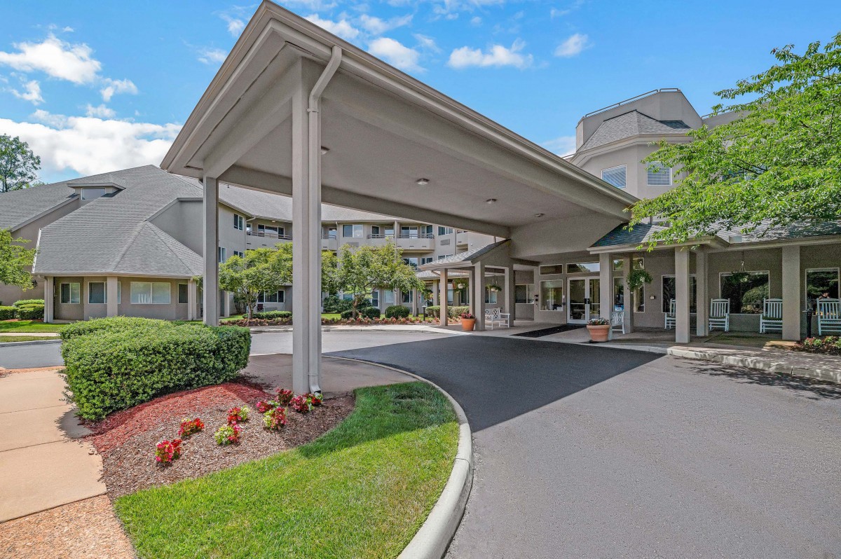 Entrance to a building with a covered driveway and landscaped surroundings.