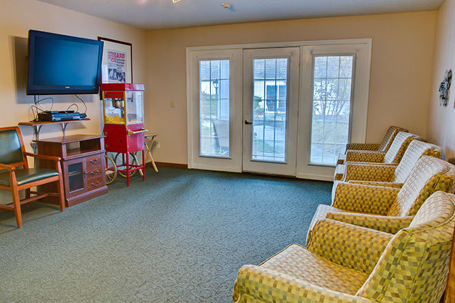 A cozy waiting room with comfortable chairs, a television, and a popcorn machine beside glass doors.