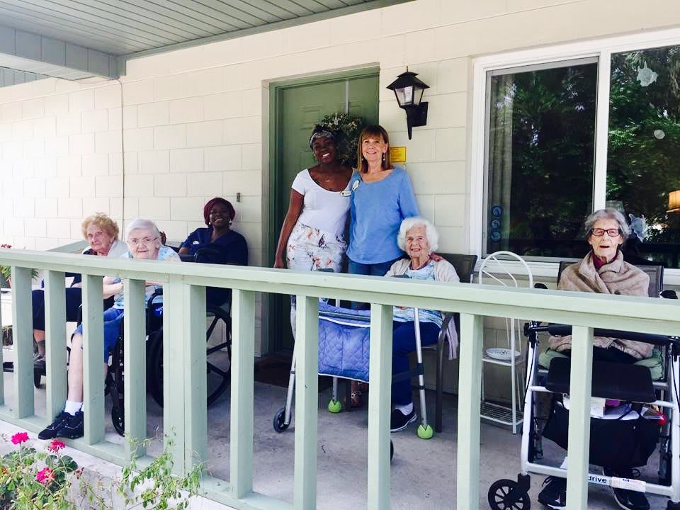 A group of elderly people and caregivers sitting on a porch enjoying the outdoors.
