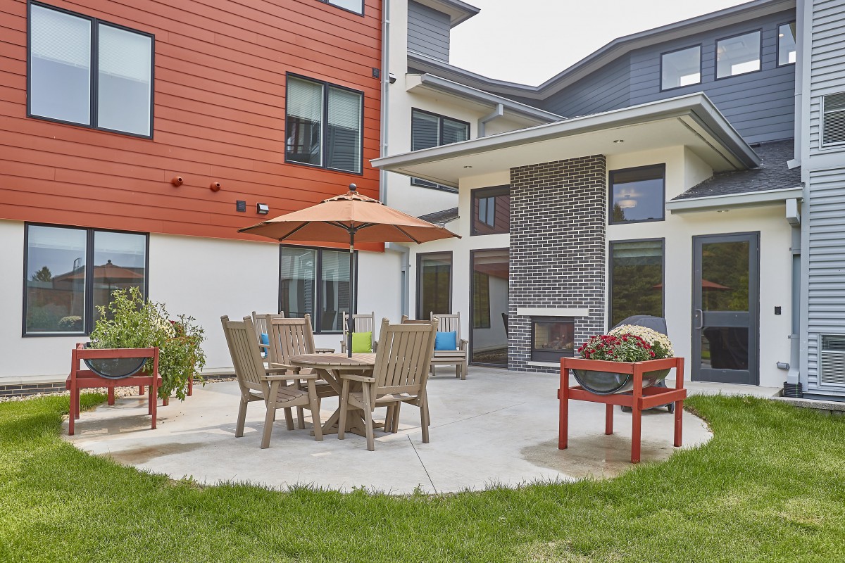 A cozy outdoor patio area with a table, chairs, and a large umbrella outside a modern building.