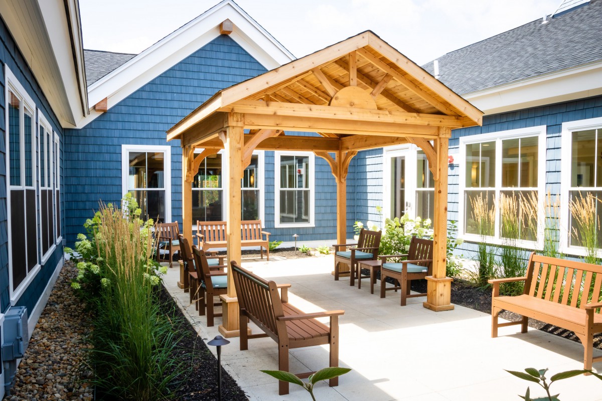 A charming patio area with a wooden pergola, surrounded by blue house exteriors and outdoor seating.