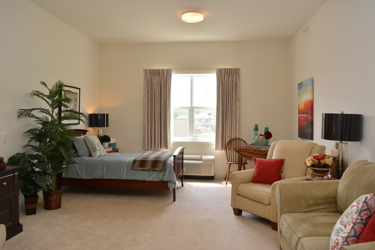A cozy bedroom with a large window, featuring a bed, armchair, and tasteful decor.