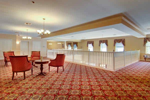 A spacious lobby area with elegant chairs and table, featuring a richly patterned carpet and multiple chandeliers.