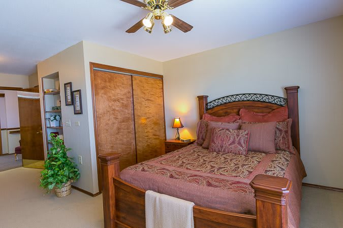 A cozy bedroom with a wooden bed, warm-toned bedding, and a ceiling fan.