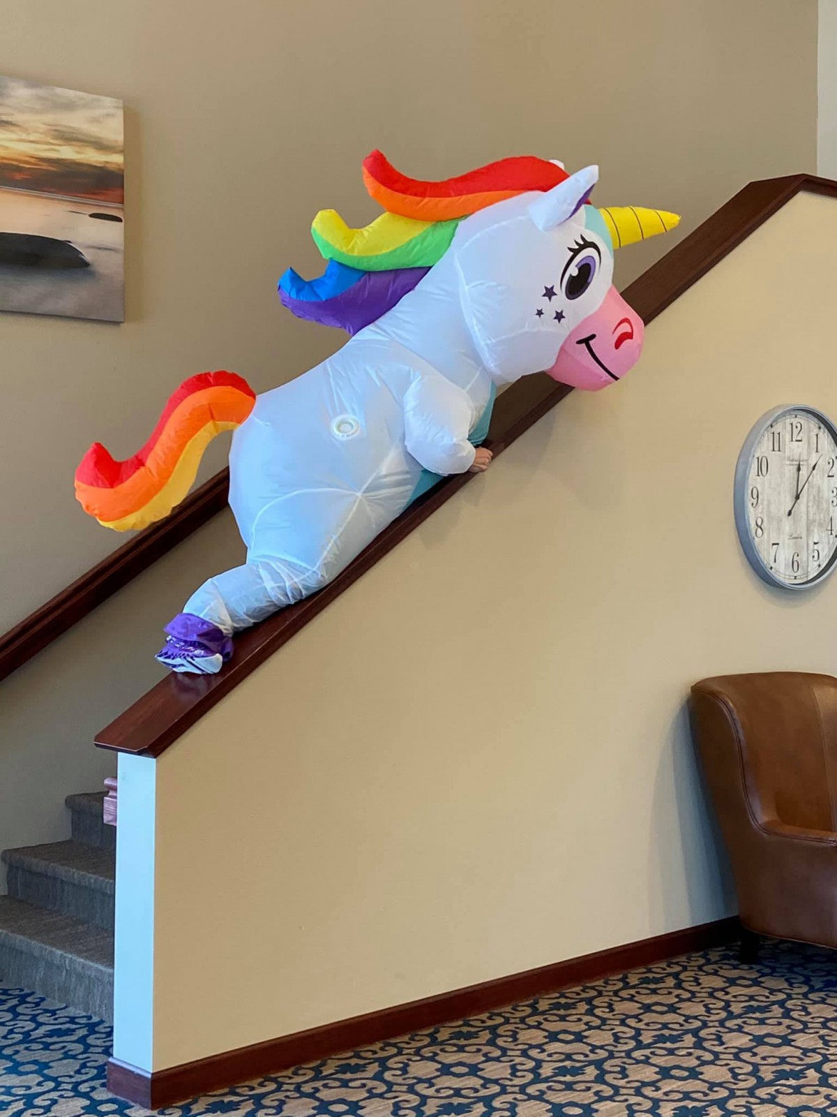 A person in a unicorn costume sliding down the stairs.