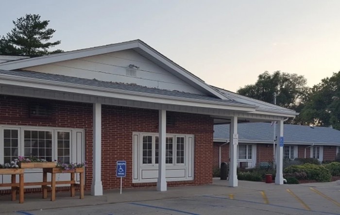 A brick building with a covered porch and adjacent parking area in the early evening light.