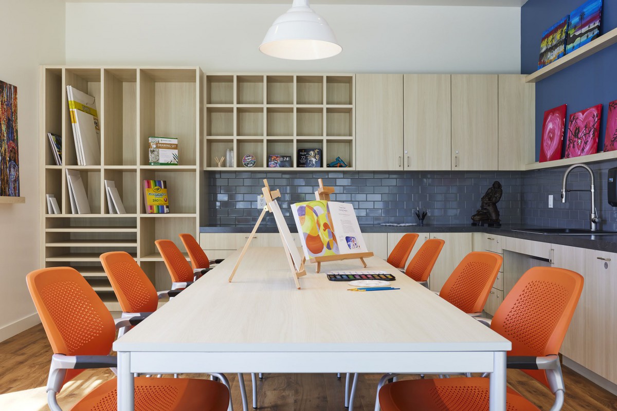 A modern meeting room with a long white conference table surrounded by orange chairs, featuring open shelves and decorative elements.