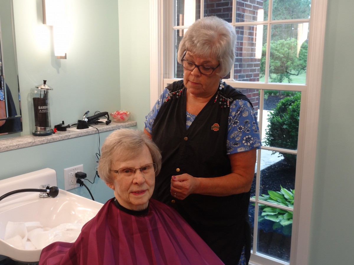 A hairstylist is giving a haircut to an elderly woman in a salon.
